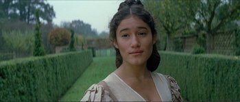 Movie still from “The New World” (2005), directed by Terrence Malick – A young woman in a dress standing in front of a hedge; Close Up shot, Low angle