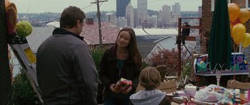 Movie still from “The Next Three Days” (2010), directed by Paul Haggis – A woman is holding a gift box while standing next to a man and a boy; Medium shot, Over the shoulder angle