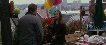 Movie still from “The Next Three Days” (2010), directed by Paul Haggis – A woman holding a bunch of balloons while standing next to a man; Medium shot, Over the shoulder angle