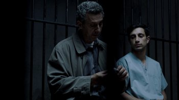 Movie still from “The Night Of” (2016), directed by James Marsh – A man in a jail cell looking at a cell phone; Medium shot, Over the shoulder angle