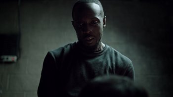 Movie still from “The Night Of” (2016), directed by James Marsh – A man in a black shirt is sitting in a dark room; Close Up shot, Low angle