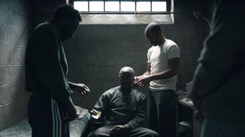 Movie still from “The Night Of” (2016), directed by James Marsh – A man sitting in a chair with two other men standing next to him; Medium shot, High angle