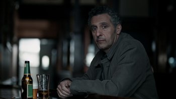 Movie still from “The Night Of” (2016), directed by James Marsh – A man sitting at a table with a glass of whiskey; Close Up shot, Over the shoulder angle
