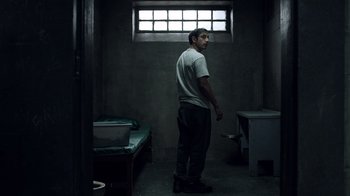 Movie still from “The Night Of” (2016), directed by James Marsh – A man standing in a room in a jail cell; Wide shot, Over the shoulder angle