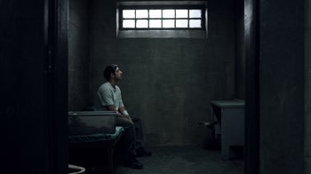 Movie still from “The Night Of” (2016), directed by James Marsh – A man sitting on a bench in a jail cell; Wide shot, High angle