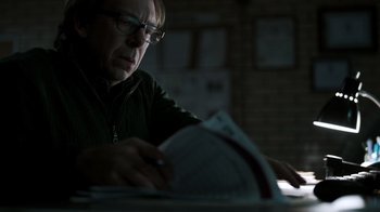 Movie still from “The Night Of” (2016), directed by James Marsh – A man sitting at a table looking at papers; Close Up shot, Over the shoulder angle