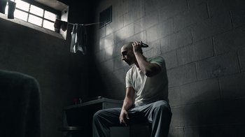 Movie still from “The Night Of” (2016), directed by James Marsh – A man sitting on a chair holding a razor; Medium shot, High angle