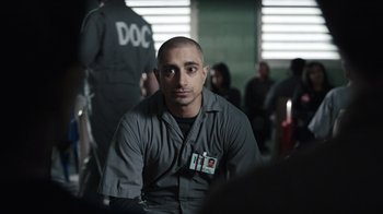 Movie still from “The Night Of” (2016), directed by James Marsh – A man in a prison uniform sitting in front of a group of people; Close Up shot, Over the shoulder angle
