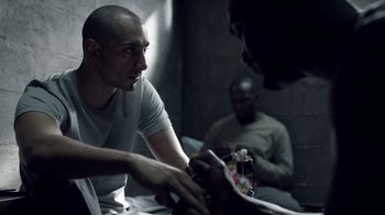 Movie still from “The Night Of” (2016), directed by James Marsh – A man sitting on a bed looking at a cell phone; Medium shot, Over the shoulder angle