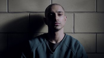 Movie still from “The Night Of” (2016), directed by James Marsh – A man in a green shirt is standing in front of a brick wall; Close Up shot, High angle