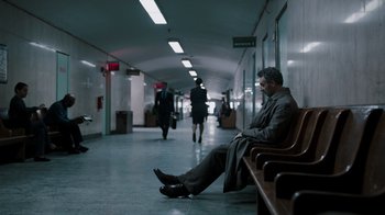 Movie still from “The Night Of” (2016), directed by James Marsh – A man sitting on top of a bench in a hallway; Wide shot, High angle