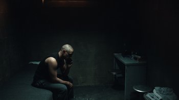 Movie still from “The Night Of” (2016), directed by James Marsh – A man sitting on a chair in a dark room; Wide shot, High angle