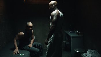 Movie still from “The Night Of” (2016), directed by James Marsh – Two men are standing in a dark room; Medium shot, Over the shoulder angle
