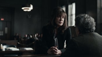 Movie still from “The Night Of” (2016), directed by James Marsh – A woman sitting at a table in front of a group of people; Medium shot, Over the shoulder angle