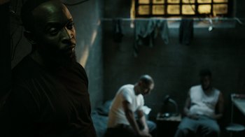 Movie still from “The Night Of” (2016), directed by James Marsh – A group of men sitting in a dark room; Medium shot, Over the shoulder angle