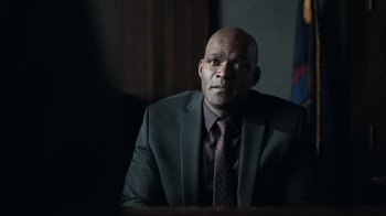 Movie still from “The Night Of” (2016), directed by James Marsh – A man wearing a suit and tie sitting at a table; Close Up shot, Over the shoulder angle
