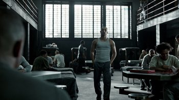 Movie still from “The Night Of” (2016), directed by James Marsh – A man standing in front of a group of people in a room; Wide shot, Over the shoulder angle