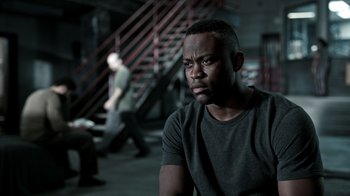 Movie still from “The Night Of” (2016), directed by James Marsh – A man sitting in front of stairs in a dark room; Close Up shot, High angle