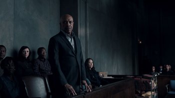Movie still from “The Night Of” (2016), directed by James Marsh – A man standing in front of two other people in a courtroom; Medium shot, Low angle