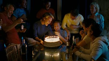 Movie still from “The Normal Heart” (2014), directed by Ryan Murphy – A group of people sitting around a table with a cake; Medium shot, High angle