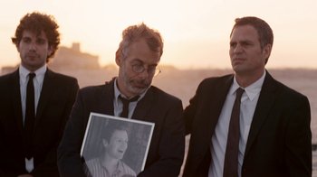 Movie still from “The Normal Heart” (2014), directed by Ryan Murphy – A man holding up a picture of a woman in front of two other men; Close Up shot, Over the shoulder angle