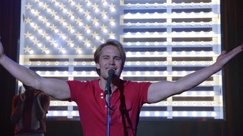 Movie still from “The Normal Heart” (2014), directed by Ryan Murphy – A man with his arms outstretched while holding a microphone in front of him; Medium shot, Low angle