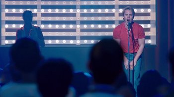 Movie still from “The Normal Heart” (2014), directed by Ryan Murphy – A man is singing into a microphone in front of a crowd; Medium shot, Low angle