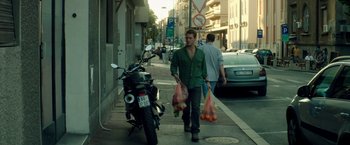 Movie still from “The November Man” (2014), directed by Roger Donaldson – A man walking down the street carrying bags of food; Wide shot, Low angle