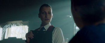 Movie still from “The November Man” (2014), directed by Roger Donaldson – A woman in a white dress shirt and tie holding a briefcase in front of a mirror; Close Up shot, Over the shoulder angle