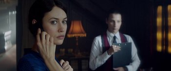 Movie still from “The November Man” (2014), directed by Roger Donaldson – A man and a woman are standing in front of a lamp; Close Up shot, Over the shoulder angle