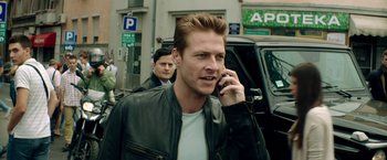 Movie still from “The November Man” (2014), directed by Roger Donaldson – A man talking on a cell phone while walking down the street; Close Up shot, Over the shoulder angle