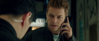 Movie still from “The November Man” (2014), directed by Roger Donaldson – A man talking on a cell phone while holding his ear buds; Close Up shot, Over the shoulder angle