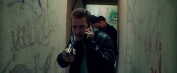 Movie still from “The November Man” (2014), directed by Roger Donaldson – A man holding a gun while talking on the phone; Medium shot, High angle