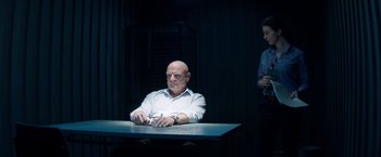 Movie still from “The November Man” (2014), directed by Roger Donaldson – A man sitting at a table in a dark room; Medium shot, Low angle