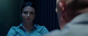 Movie still from “The November Man” (2014), directed by Roger Donaldson – A woman sitting in front of a man in front of a curtain; Close Up shot, Over the shoulder angle