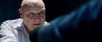 Movie still from “The November Man” (2014), directed by Roger Donaldson – An older bald man looking at the camera; Close Up shot, Over the shoulder angle
