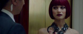 Movie still from “The November Man” (2014), directed by Roger Donaldson – A woman with red hair holding a magnifying glass in front of a mirror; Close Up shot, Over the shoulder angle