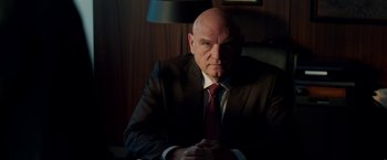 Movie still from “The November Man” (2014), directed by Roger Donaldson – A man in a suit and tie sitting in a chair; Close Up shot, Low angle