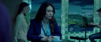 Movie still from “The November Man” (2014), directed by Roger Donaldson – A woman sitting at a table with a cup of coffee; Medium shot, Over the shoulder angle