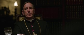 Movie still from “The Nun” (2018), directed by Corin Hardy – A man wearing a black suit and a gold chain; Close Up shot, Low angle
