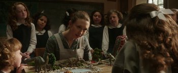 Movie still from “The Nun” (2018), directed by Corin Hardy – A group of people standing around a table with food on top of it; Medium shot, Over the shoulder angle