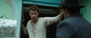 Movie still from “The Nun” (2018), directed by Corin Hardy – A man in a white shirt is standing in front of a blue wall; Medium shot, Low angle