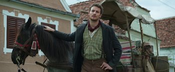 Movie still from “The Nun” (2018), directed by Corin Hardy – A man standing next to a brown horse; Medium shot, Low angle