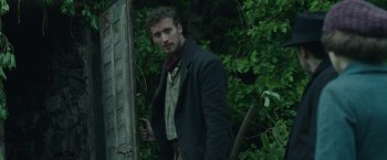 Movie still from “The Nun” (2018), directed by Corin Hardy – A man standing in front of a door in a wooded area; Medium shot, Low angle