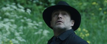 Movie still from “The Nun” (2018), directed by Corin Hardy – A man wearing a black hat and a black shirt; Close Up shot, Low angle