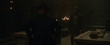Movie still from “The Nun” (2018), directed by Corin Hardy – A man in a black coat and a man in a black hat; Medium shot, Over the shoulder angle