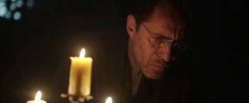 Movie still from “The Nun” (2018), directed by Corin Hardy – A man with glasses is looking at a candle; Close Up shot, Low angle