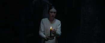 Movie still from “The Nun” (2018), directed by Corin Hardy – A woman holding a candle in a dimly - lit room; Medium shot, High angle