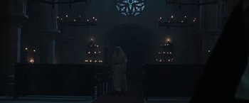 Movie still from “The Nun” (2018), directed by Corin Hardy – A person standing in front of candles in a dark room; Wide shot, Low angle