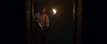 Movie still from “The Nun” (2018), directed by Corin Hardy – A man holding a burning torch in a dark room; Medium shot, Low angle